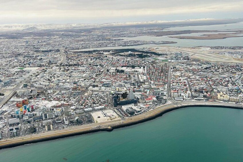 Una vista aerea di una città costiera con un porto importante, un'area urbana densa e una catena montuosa in lontananza. 2