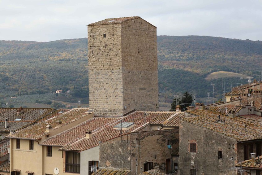 A historic stone tower in a village with terracotta roofs and a mountainous backdrop. 1