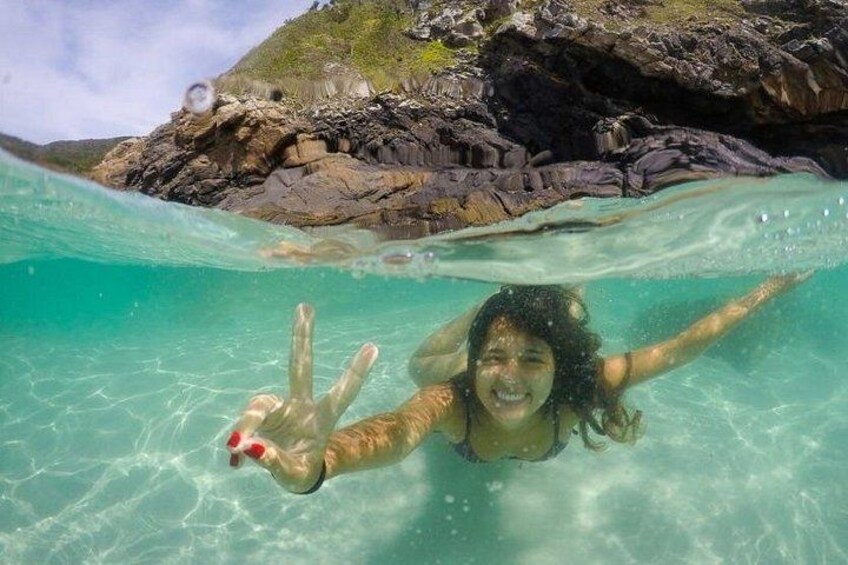A person swimming underwater with clear turquoise water and rocky formations in the background. 2