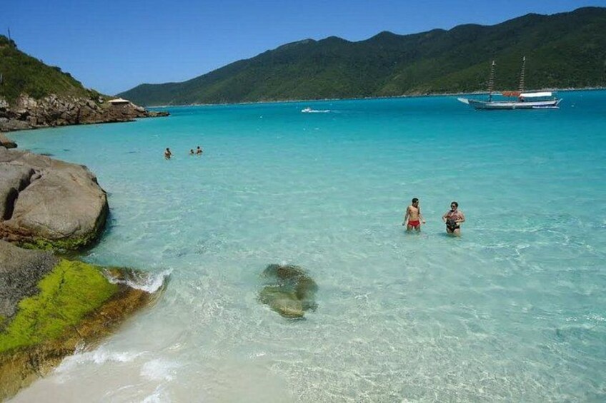 A coastal scene with clear turquoise water, rocky shore, and a boat in the distance. 3