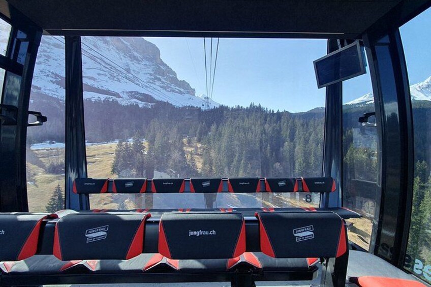Et bilinteriør med sæder mærket 'jungfrau.ch' og udsigt til et bjerglandskab med sneklædte tinder og tætte skove. 2