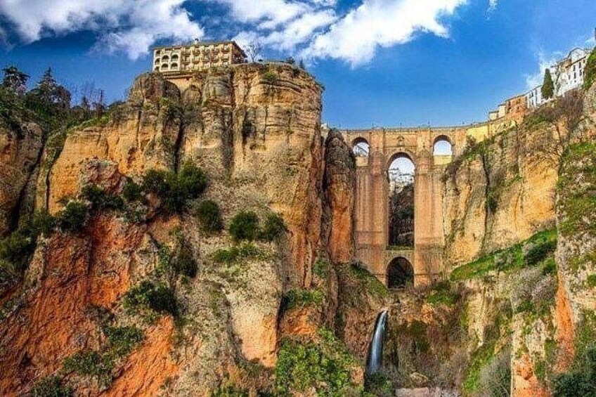 A historical stone bridge with arches, a castle on a cliff, and a waterfall. 2