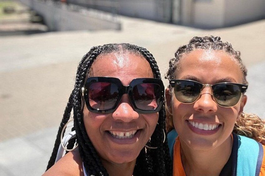 Two people with braided hair, one wearing sunglasses, standing outdoors. 2