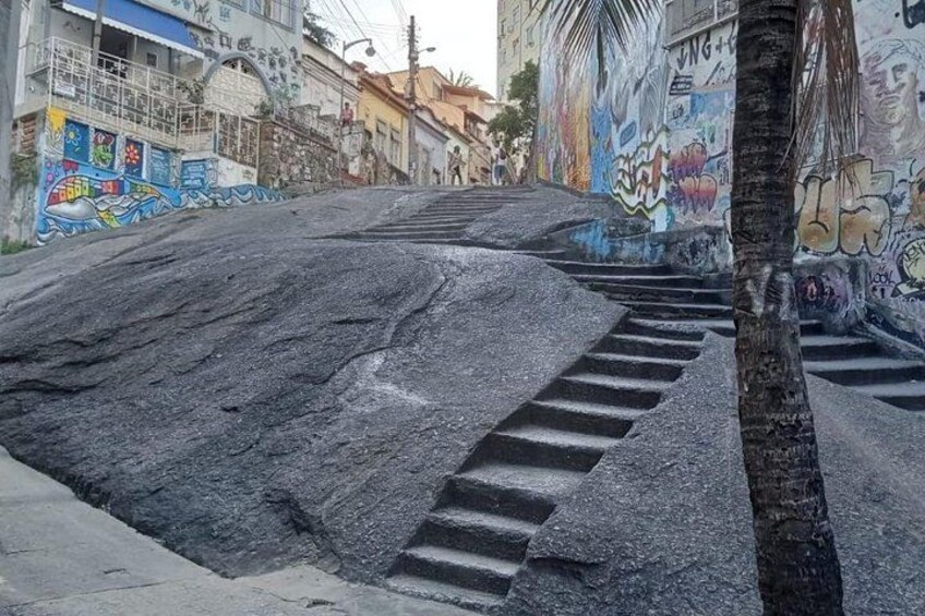 A street with graffiti on walls, a palm tree, and steps leading up a hill. 5