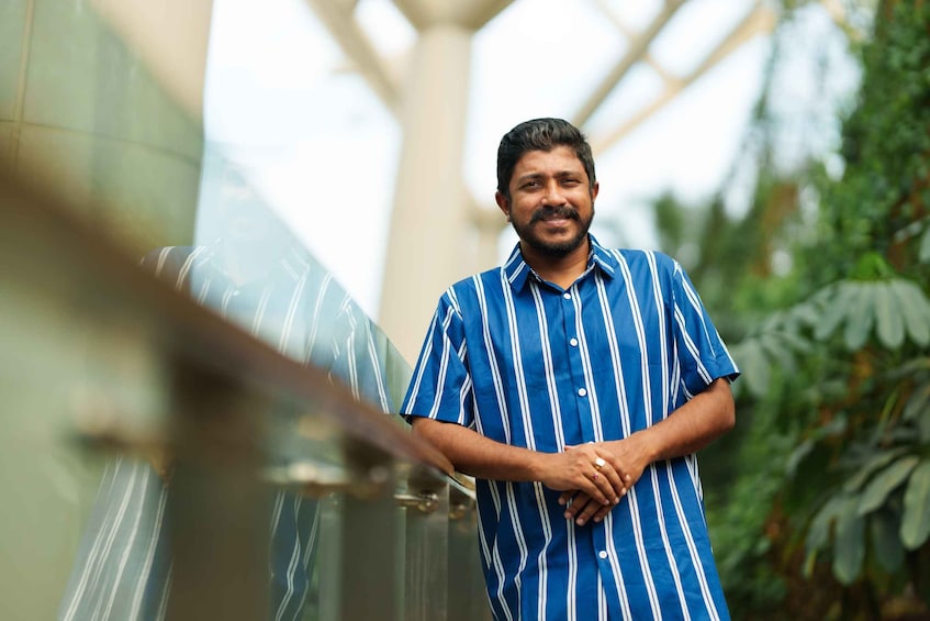 A person in a blue striped shirt standing in a corridor with glass walls and greenery. 2
