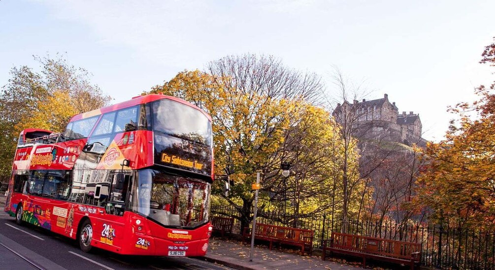A red double-decker bus on a road with autumn trees and a castle in the background. 2