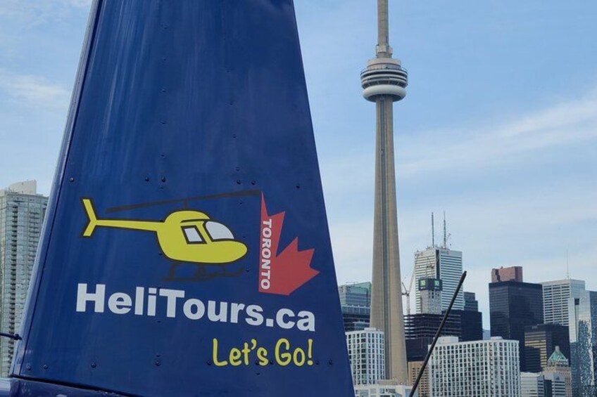 A blue helicopter with 'HeliTours.ca' and 'Let's Go!' on a city skyline with the CN Tower. 2