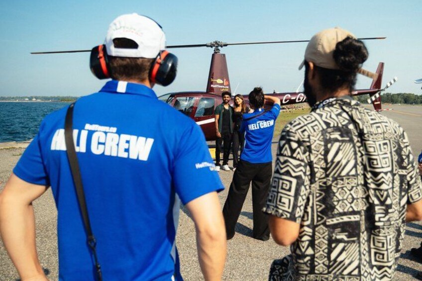 A helicopter with a crew member in a blue shirt labeled 'HILICREW' and another in a patterned shirt standing by. 5