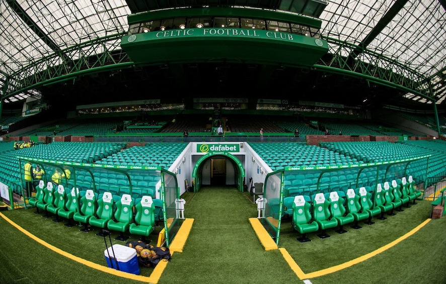 An indoor stadium with green seating, a roof structure, and a sign for 'Celtic Football Club'. 3