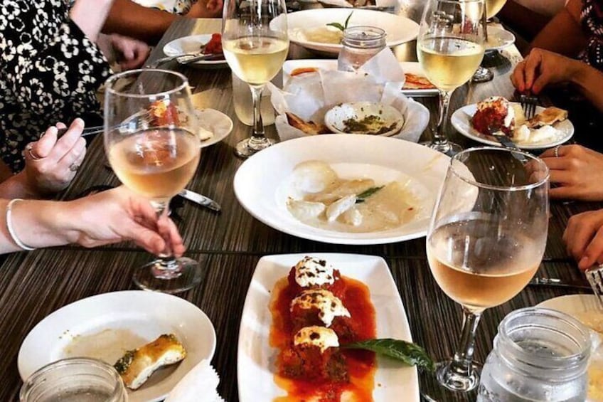Un tavolo da pranzo imbandito con piatti di cibo, bicchieri di vino e persone che mangiano. 2