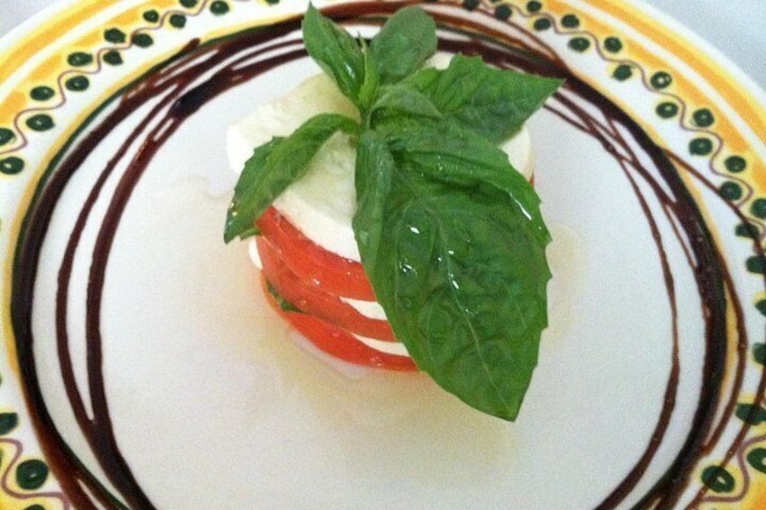 Un piatto con pomodoro, mozzarella e basilico su una piastra bianca con bordo decorativo. 4