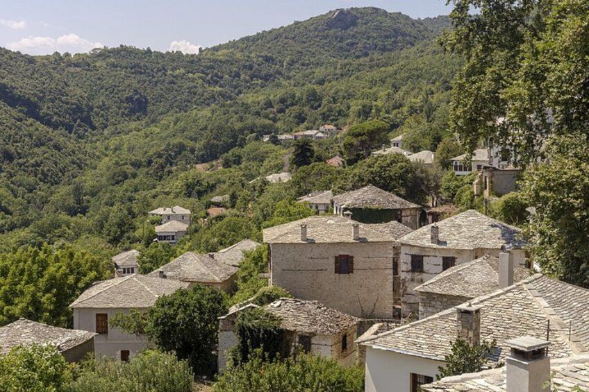 A hillside village with traditional stone houses, lush greenery, and a mountain in the background. 2