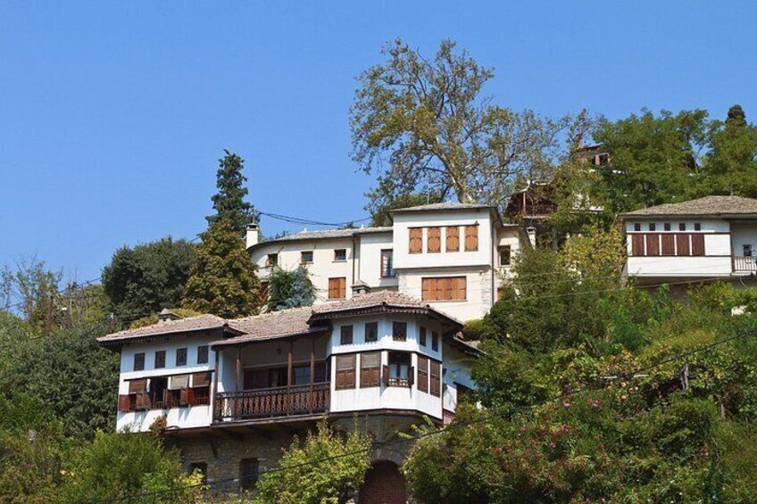 A hillside residential area with multi-story houses, lush greenery, and a clear blue sky. 4