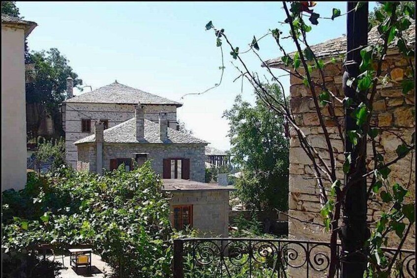 A stone building with a tiled roof, surrounded by greenery and a wrought iron fence. 5