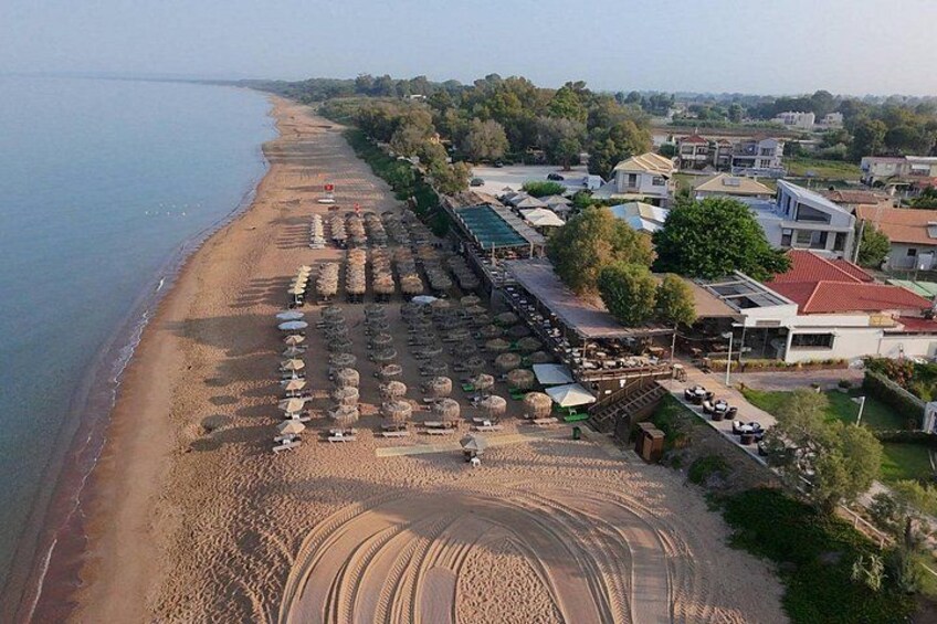 A beach with rows of umbrellas and sunbeds, a sandy shore, and buildings in the background. 2