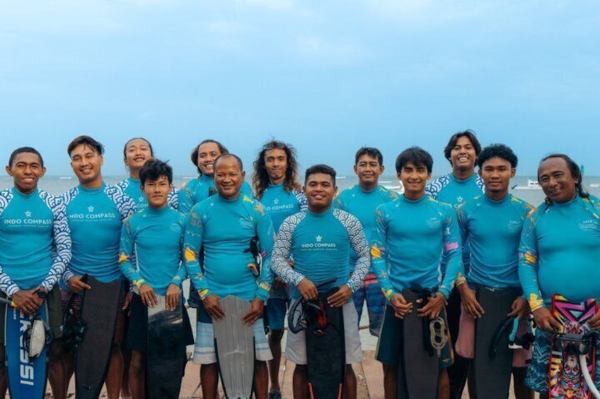Eine Gruppe von Personen in blauen Hemden mit der Aufschrift 'INDO COMPASS', die auf einem Strand stehen. 2