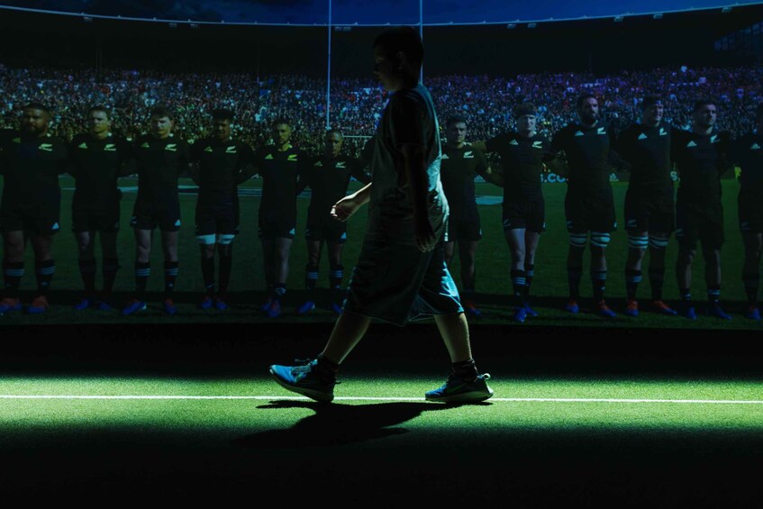 Una persona caminando sobre un campo de fútbol iluminado, con un público en el fondo. 5