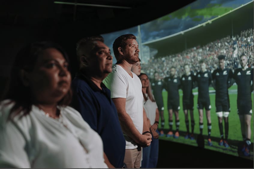 Un grupo de personas observando una pantalla grande que muestra un evento deportivo. 1