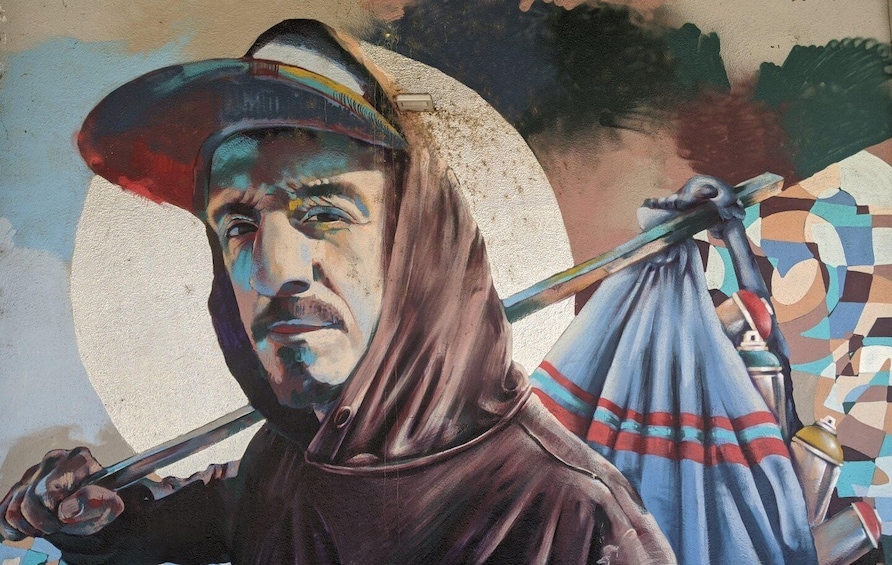 A mural of a figure holding a staff and a bag, with a circular pattern in the background. 3