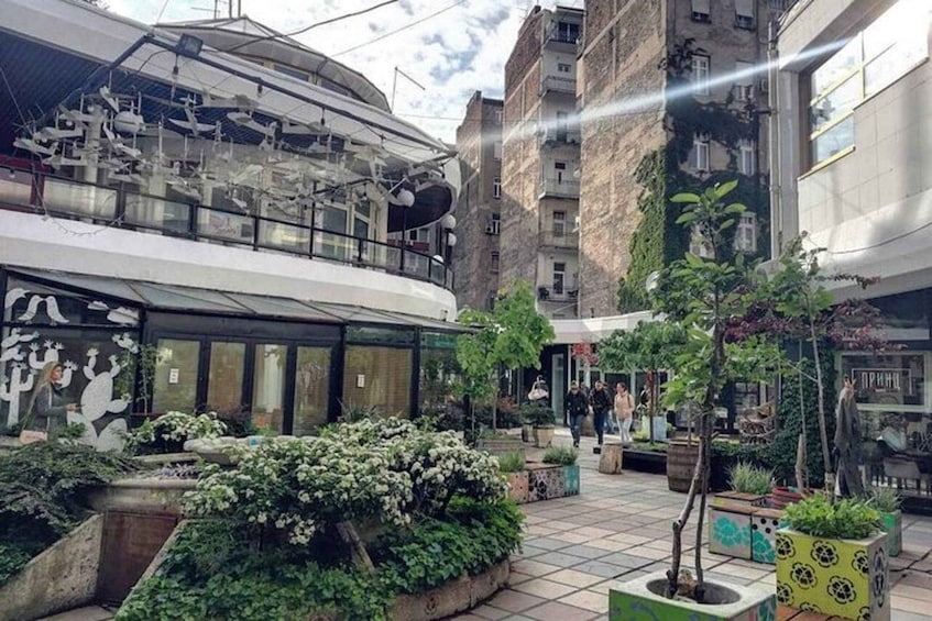A courtyard with potted plants, a building with a glass facade, and a staircase. 1