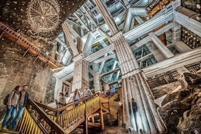 An interior with a large wooden staircase, a central circular structure, and a high ceiling with beams. 1