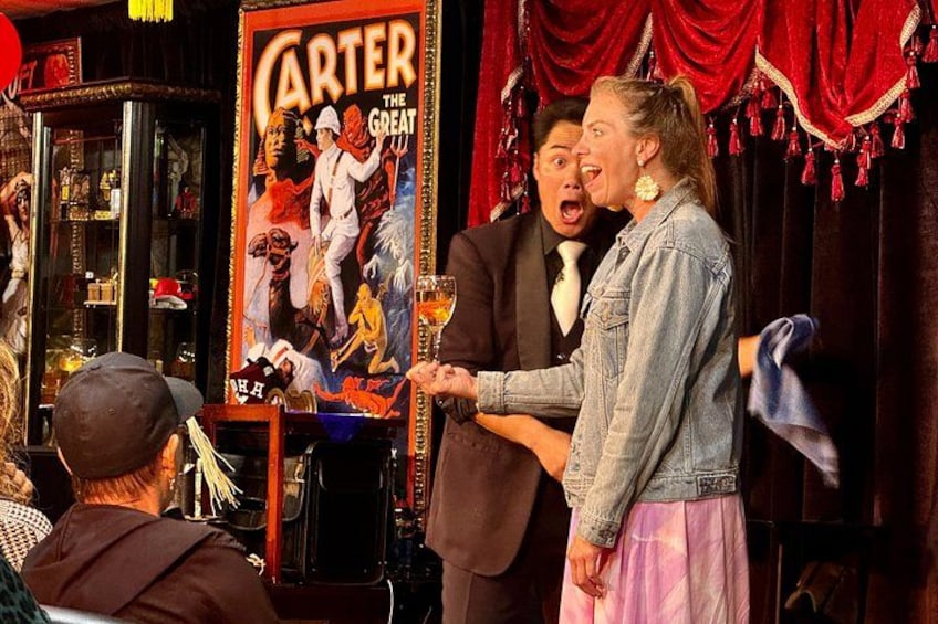 A bar scene with a poster of 'Carter the Great' and a man in a suit shaking hands with a woman in a denim jacket. 2
