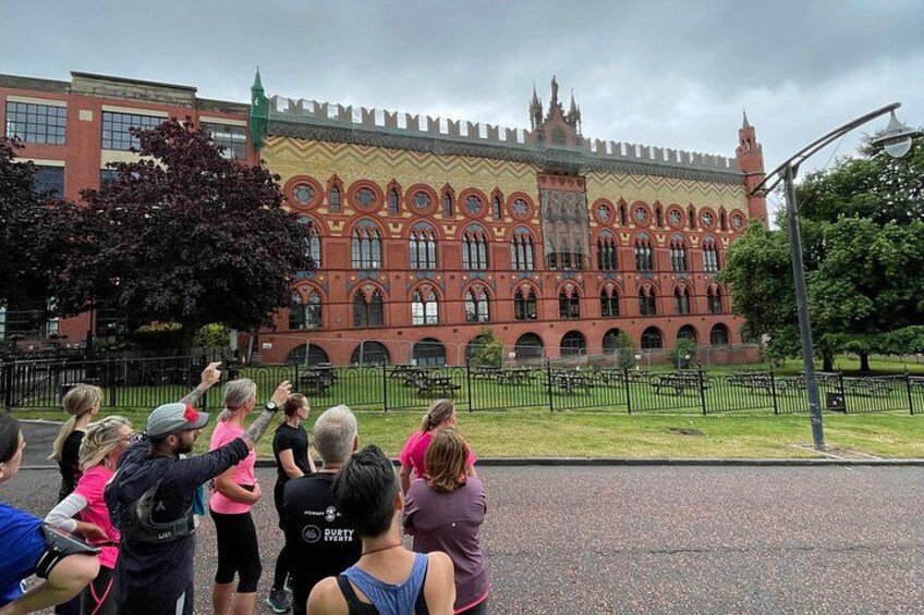 Un groupe de personnes se tient devant un grand bâtiment orné, à la façade rouge et aux nombreuses fenêtres. 3
