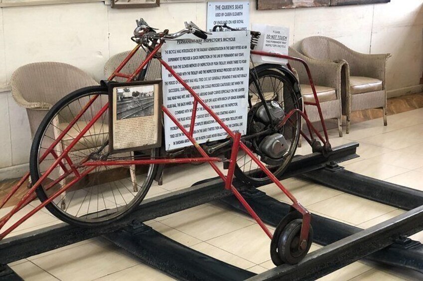 Een rode fiets met een bord over de geschiedenis, een stoel en een tafel in een museum. 3