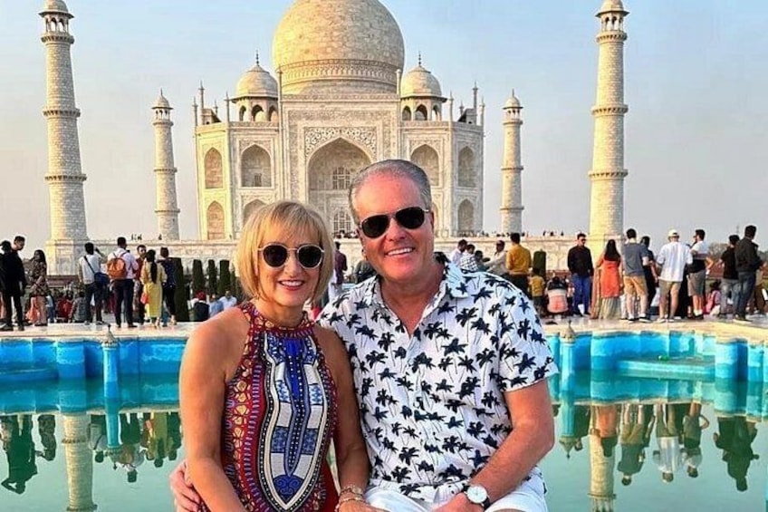 A couple standing in front of the Taj Mahal with a reflection in the water. 1