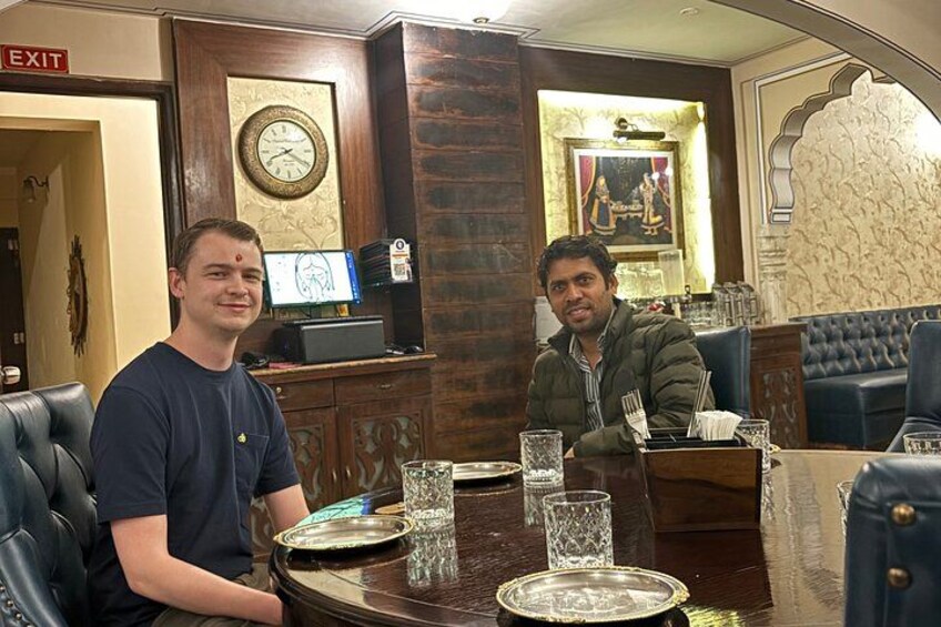 Two men seated at a table in a restaurant with a clock and a framed picture on the wall. 3