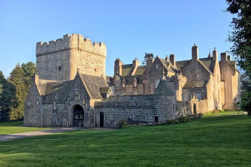 Un castillo histórico con una torre destacada, muros de piedra y un césped bien cuidado. 4