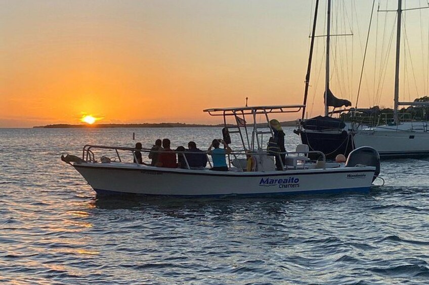 Un bote con gente a bordo, una puesta de sol al fondo y agua tranquila. 5