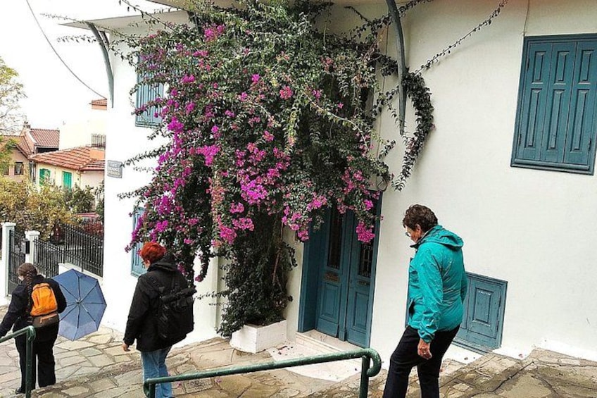 Un edificio con un árbol de flores rosadas, una puerta azul y una persona con una chaqueta verde azulado cerca de la entrada. 4
