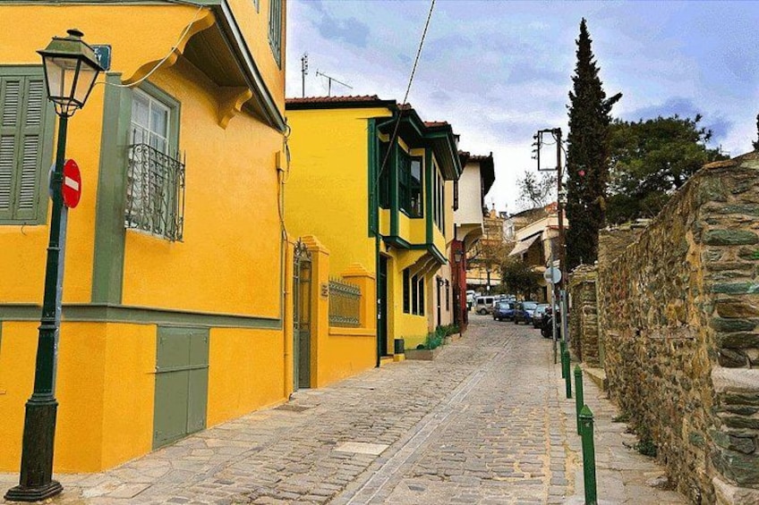Una calle adoquinada flanqueada por edificios coloridos, un muro de piedra y un farol. 2