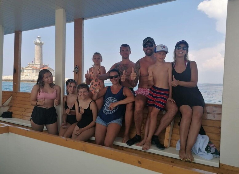 En grupp människor står på ett trädäck med utsikt över havet, och i bakgrunden syns en fyr. 3