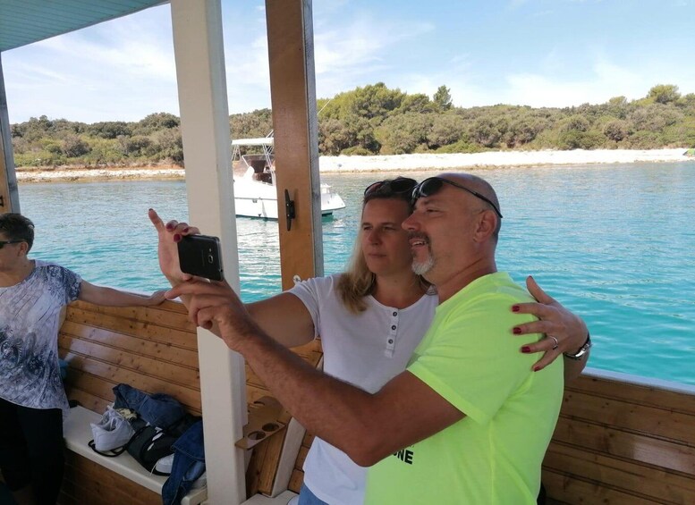 En träbåt med människor som tar en selfie, ett lugnt hav och en kustlinje med träd. 5