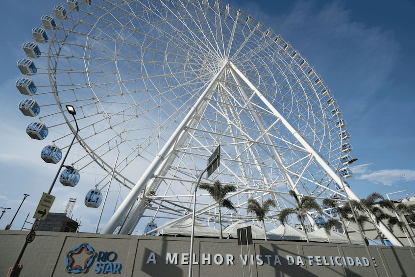 A Ferris wheel with gondolas, palm trees, and a sign that reads 'RIO STAR A MELHOR VISTA DA FELICIDADE.' 3