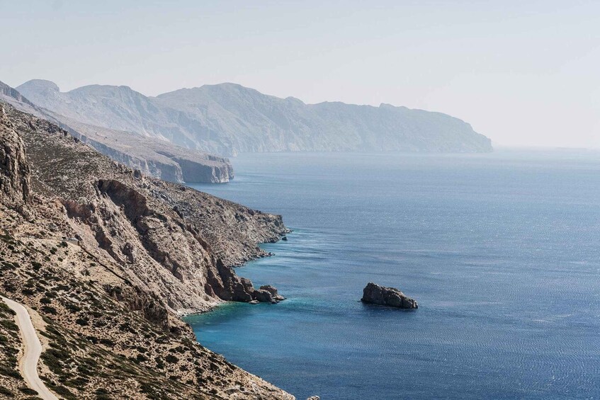 Una carretera costera serpentea a lo largo de un acantilado rocoso, con vista despejada al mar y montañas distantes. 5