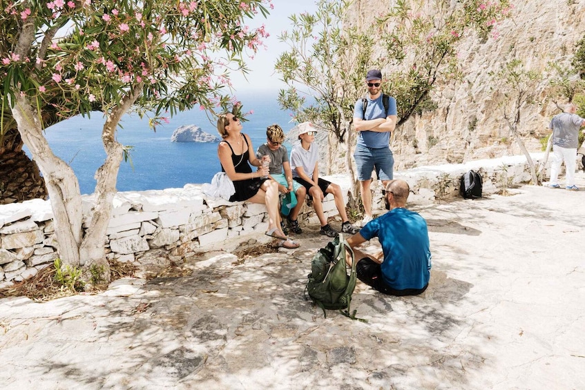 Un grupo de personas sentadas y de pie en un sendero de piedra junto al mar, con vista al océano y acantilados rocosos. 4