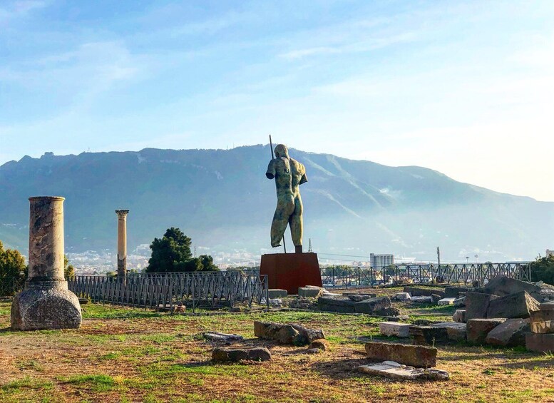 A statue on a pedestal, ancient columns, and ruins in a historical site with mountains in the background. 1