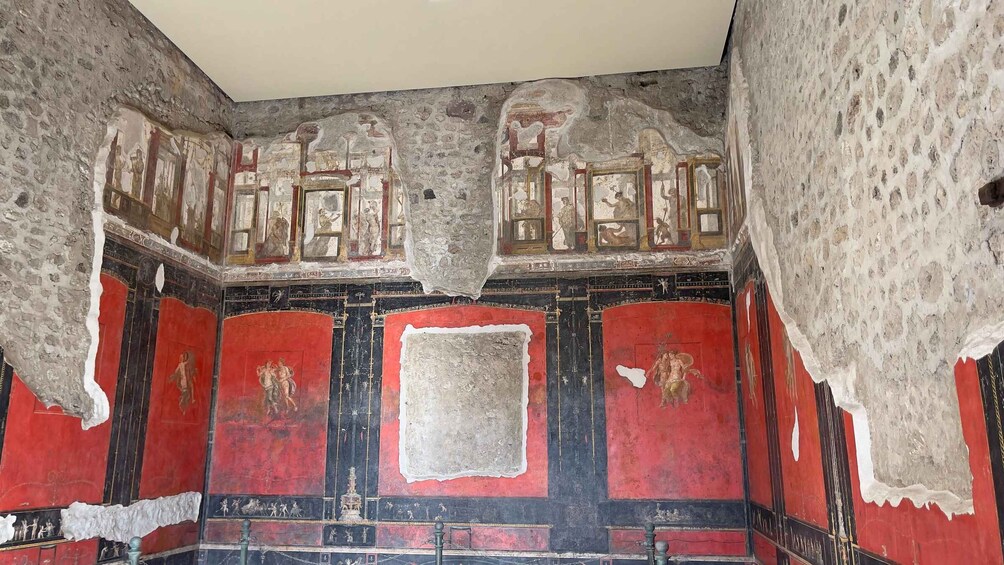 An ancient Roman fresco with red and black walls, depicting figures and architectural elements. 3