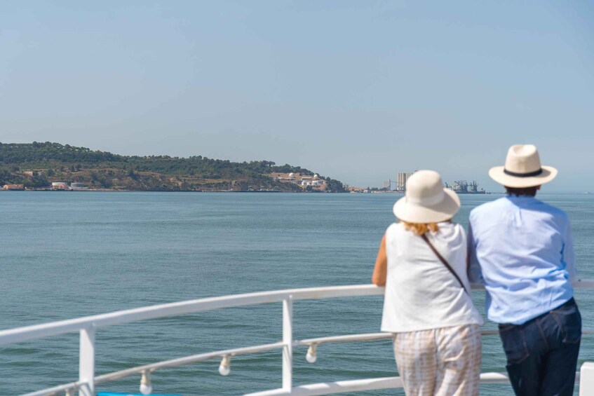 Dos personas en un bote, observando un paisaje costero con edificios y una colina. 2