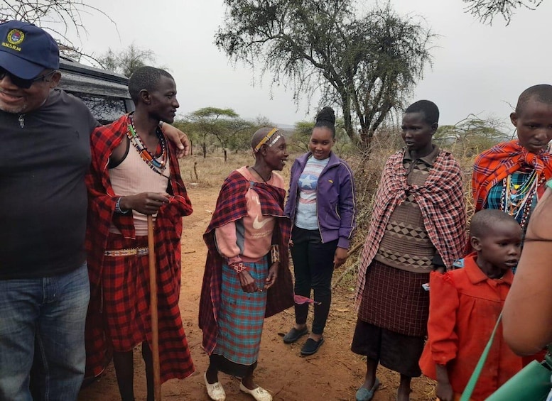 Un groupe de personnes se trouve dans un cadre rural, avec des arbres et un véhicule en arrière-plan. 2