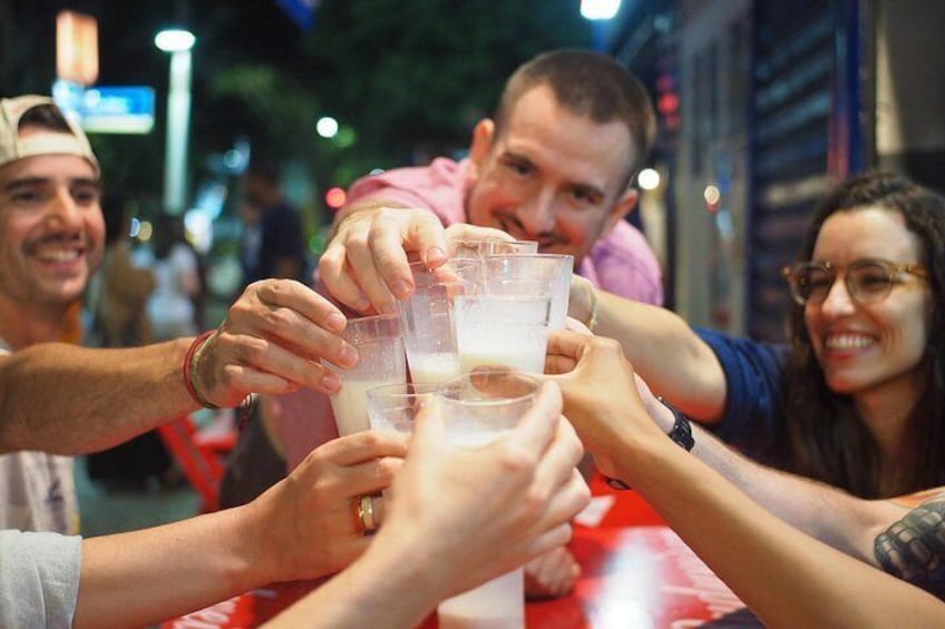Personas brindando con bebidas en una mesa, en un espacio público. 1