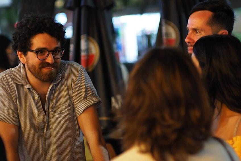 Una persona con camisa a rayas parada en un espacio público con un fondo desenfocado. 4