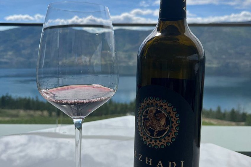 Una copa de vino con una botella de ZHADI, una vista panorámica de montañas y un lago al fondo. 3