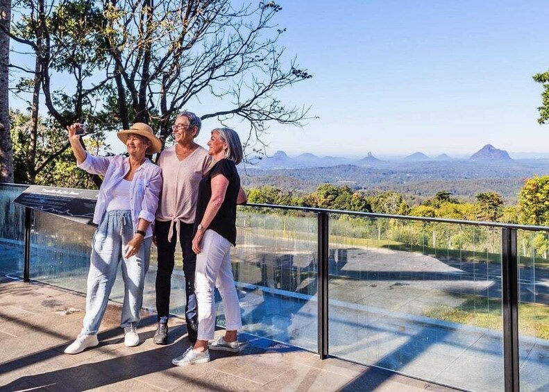 Three people taking a selfie on a balcony with a scenic view of mountains and trees. 1