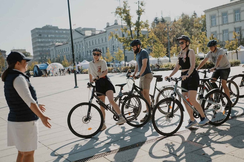 A group of people on bicycles in an urban setting with buildings and trees in the background. 1