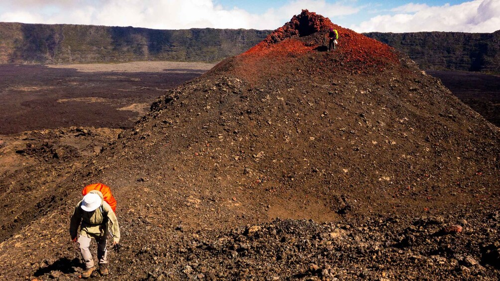A hiker on a rocky terrain with a large pile of red material in the background. 1