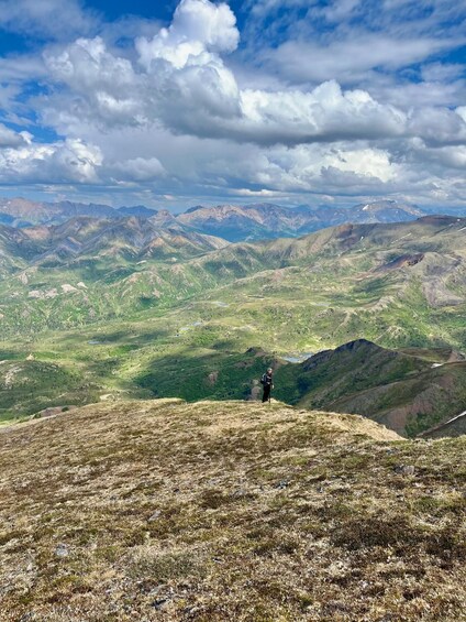A hiker on a mountain ridge with expansive views of a valley and distant mountains under a partly cloudy sky. 2